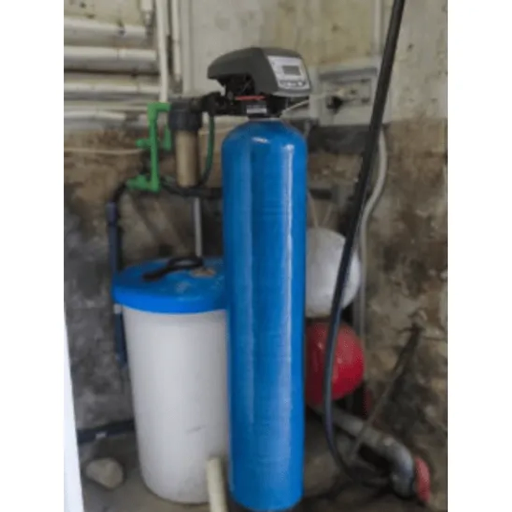 Homeowner adding salt pellets from a yellow bucket into an open cabinet-style water softener tank during routine maintenance