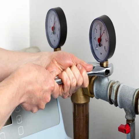 Maintenance on a water softener or filtration system, showing gauges and pipe work being adjusted.