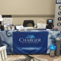Charger Water Treatment Products exhibit table with logo banner and sample water filtration components.