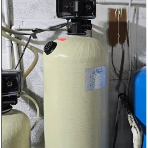 Crystal Water Plumbing water softener.png showing a high-capacity residential water softener with a light-tan textured fiber-wound resin tank and an attached "Water Tender" service specifications label