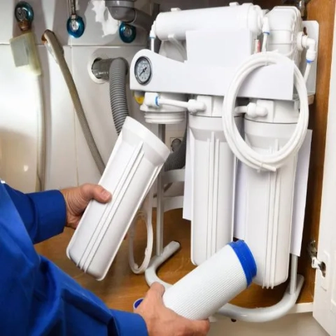 Technician installing replacement filters in a multi-stage under-sink reverse osmosis (RO) water filtration system.