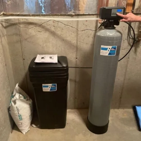 Ken Neyer Plumbing installed water softener system with resin tank, brine tank, and salt bag in a home basement.