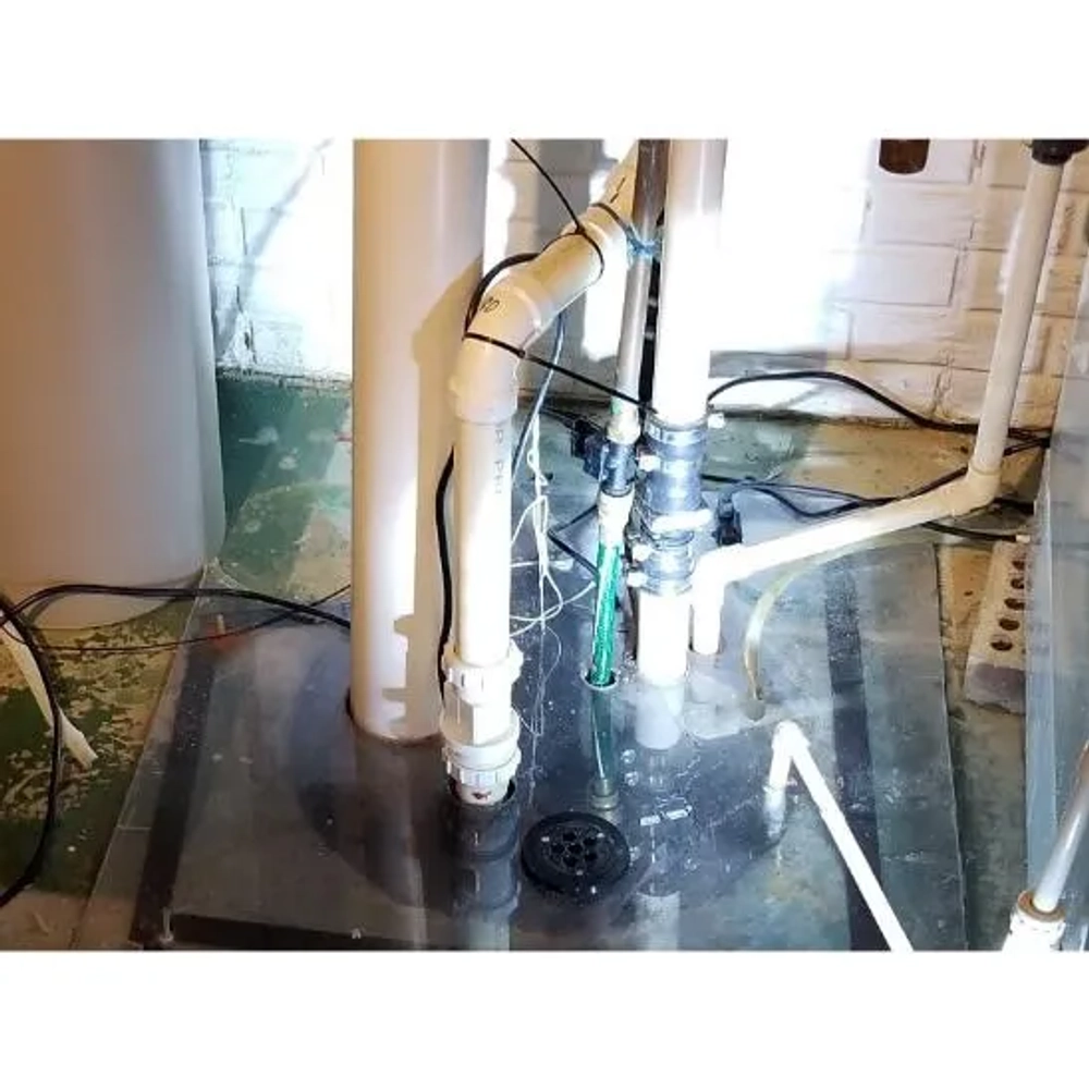 Close-up of a basement sump basin with white piping and pump inlet for drainage service.