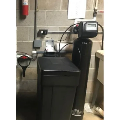 Home water treatment: large black water softener unit with a digital timer head and a nearby fire extinguisher.