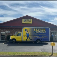 Yellow Seiter Services truck parked outside their office offering heating, AC, and plumbing.