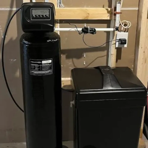 A black Superior Water Treatment water softener system installed in a residential basement