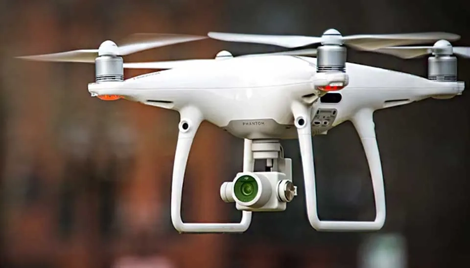 Photograph of the DJI Phantom 4 Pro drone, a white quadcopter with four propellers. The image prominently displays the 3-axis gimbal stabilizing a camera underneath the drone's body. The drone's design appears sturdy and professional, reflecting its use in applications like water quality monitoring and surveying, as discussed in the article