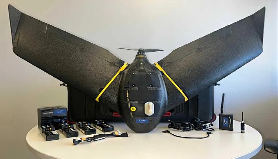 Photograph displaying the SenseFly eBee X fixed-wing drone along with a comprehensive set of its interchangeable sensor payloads.  Visible are several different sensor modules, identifiable by varying shapes and lens configurations, likely representing the senseFly S.O.D.A. 3D, Aeria X, Duet T, MicaSense RedEdge-MX, and Parrot Sequoia+.