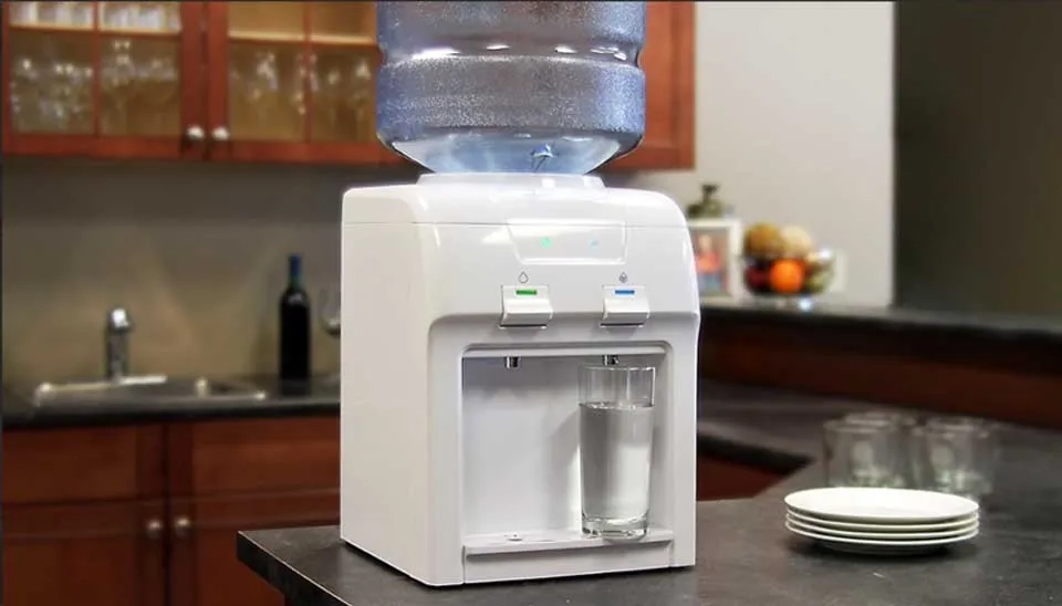 A glass is being filled with water from the Vitapur Countertop Top Loading Water Dispenser.