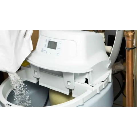 A white water softener system being refilled with salt, showing the digital control panel and pipes.