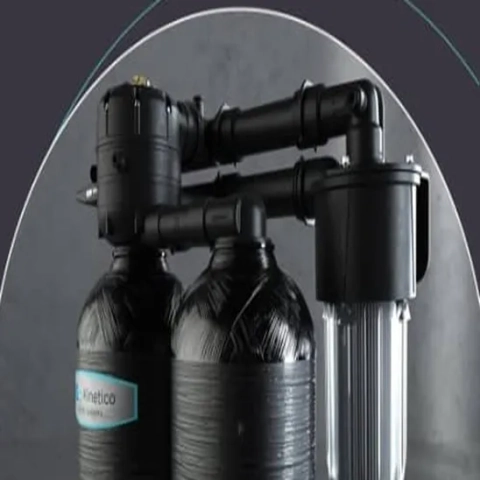 Kinetico twin-tank water softener plumbing with control valve and transparent pre-filter housing.